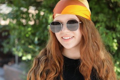 Photo of Portrait of happy teenage girl with long hair wearing sunglasses and bandana outdoors