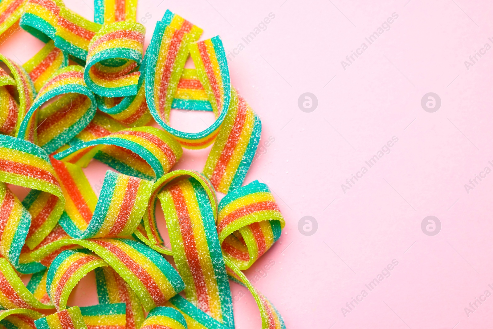 Photo of Tasty rainbow sour belts on pink background, top view. Space for text