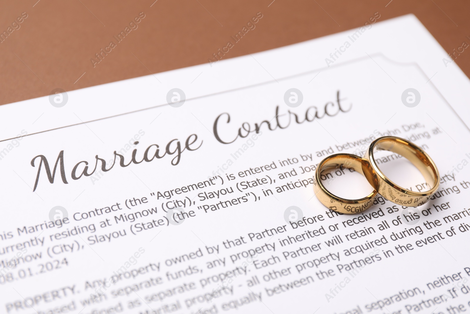 Photo of Marriage contract and golden rings on brown background, closeup