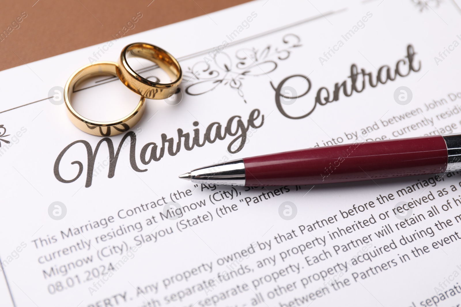 Photo of Marriage contract, pen and golden rings on brown background, closeup