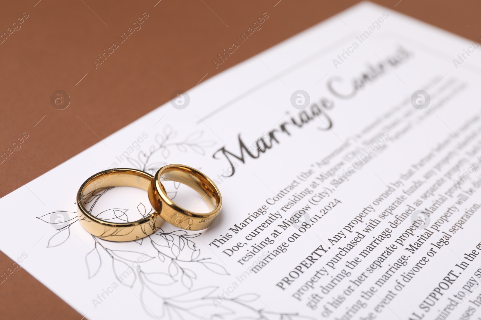 Photo of Marriage contract and golden rings on brown background, closeup