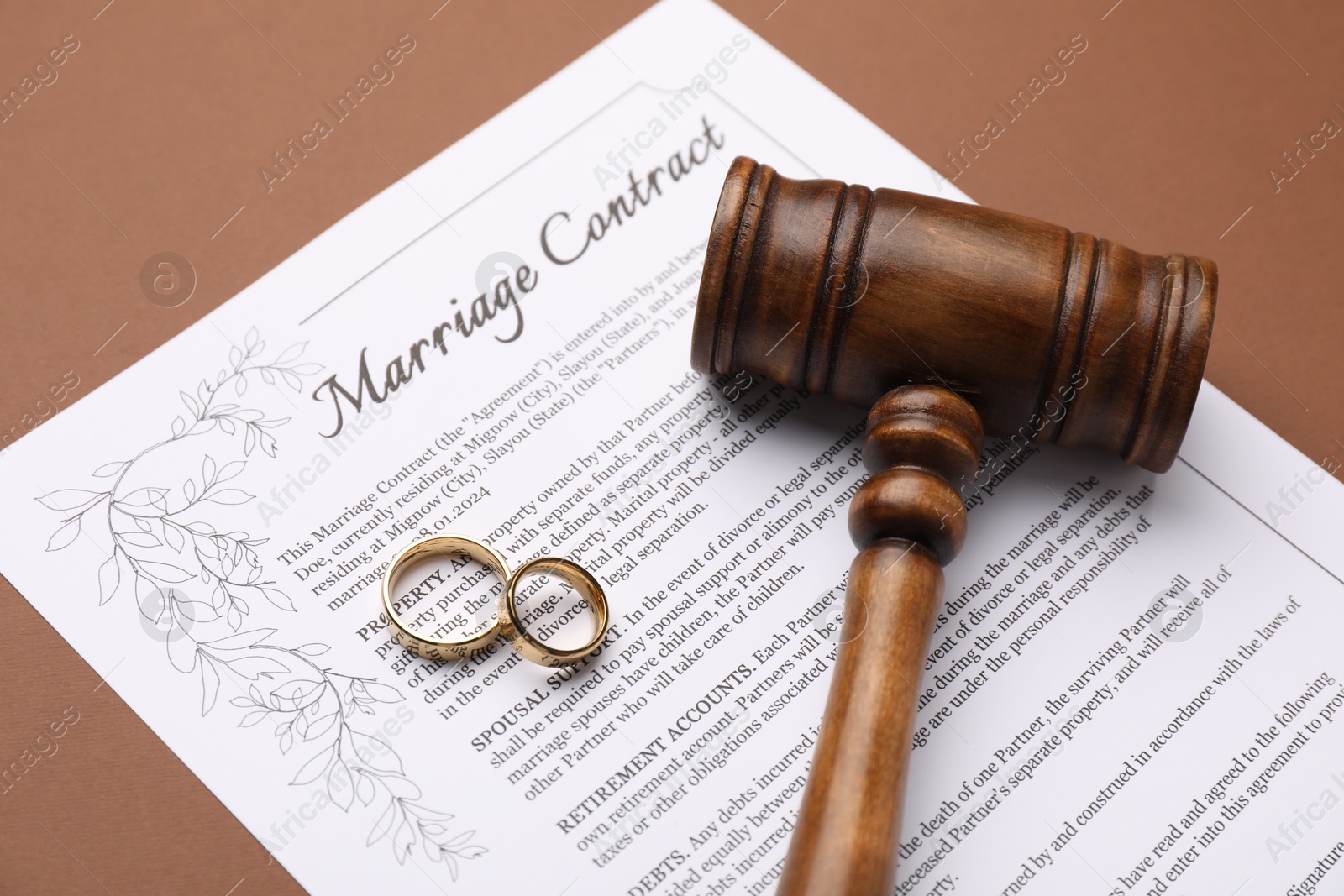 Photo of Marriage contract, gavel and golden rings on brown background, closeup