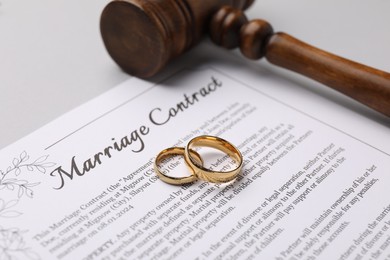 Photo of Marriage contract, gavel and golden rings on light grey background, closeup