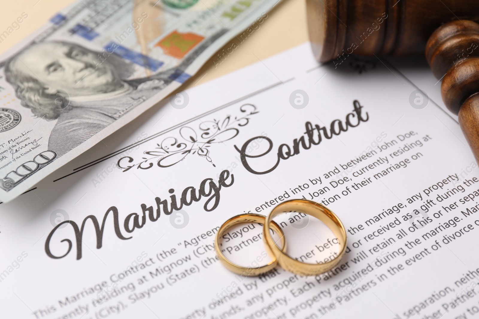 Photo of Marriage contract, gavel, dollar bill and golden rings on beige background, closeup