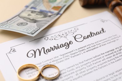 Photo of Marriage contract, gavel, dollar bill and golden rings on beige background, closeup