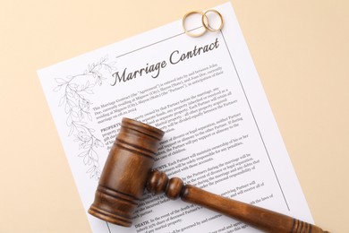 Photo of Marriage contract, gavel and golden rings on beige background, top view