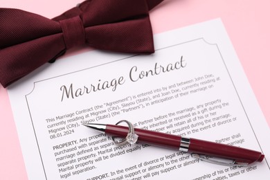 Photo of Marriage contract, bowtie, pen and ring on pink background, above view