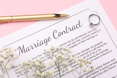 Marriage contract, flowers, pen and ring on pink background, top view