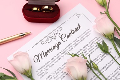 Photo of Marriage contract, flowers, pen and golden rings on pink background, above view