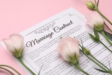 Photo of Marriage contract and flowers on pink background, closeup