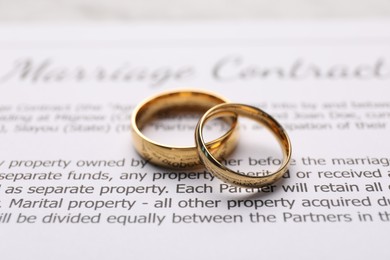 Photo of Marriage contract and stylish golden rings, closeup