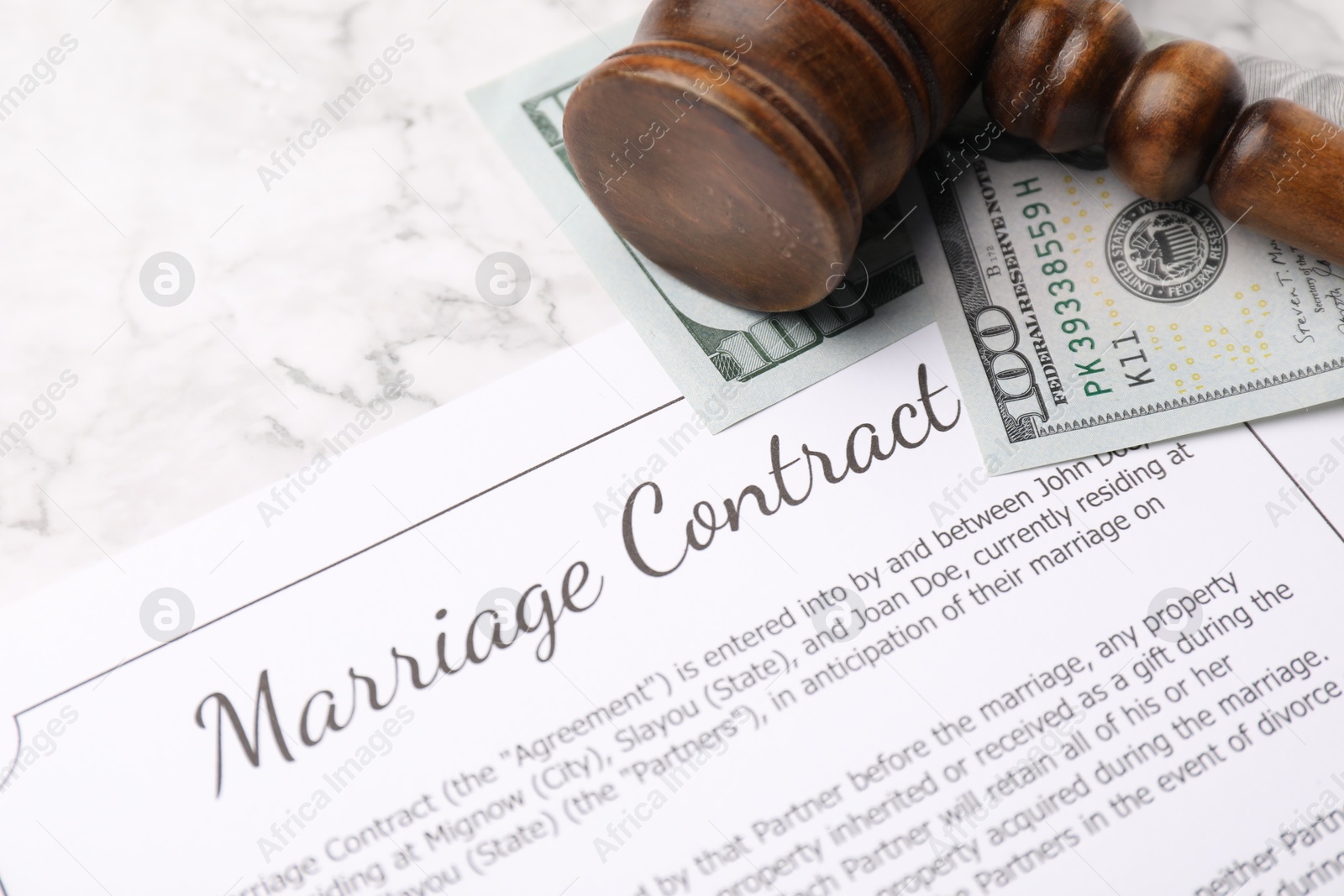 Photo of Marriage contract, dollar bill and gavel on white marble table, closeup