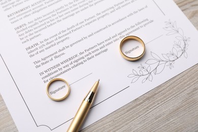 Photo of Marriage contract, pen and golden rings on light wooden table, above view