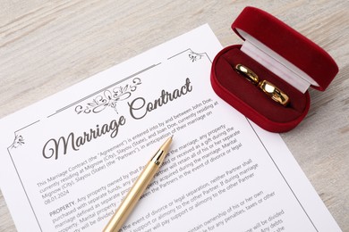 Photo of Marriage contract, pen and golden rings on light wooden table, top view