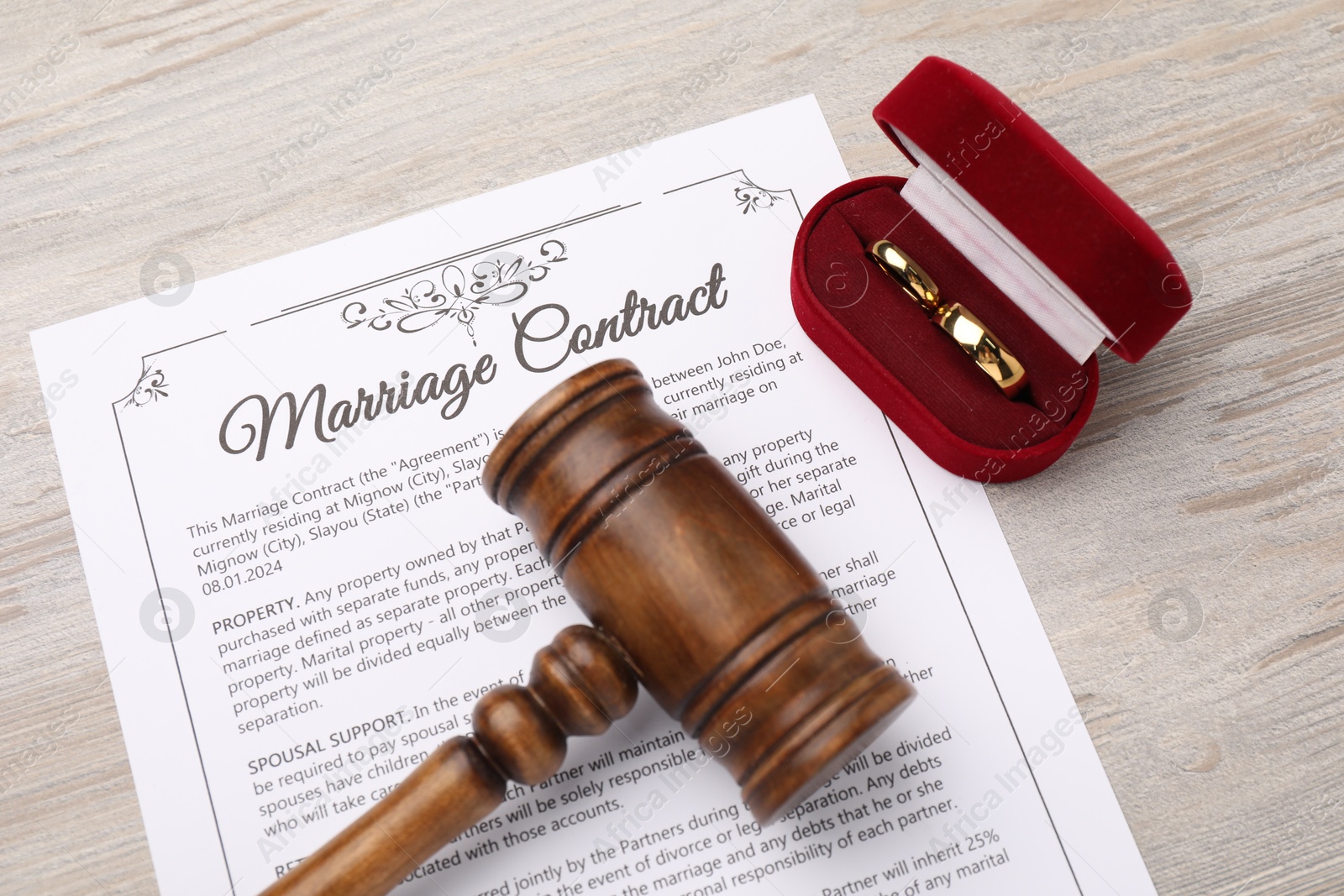 Photo of Marriage contract, gavel and golden rings on light wooden table, top view