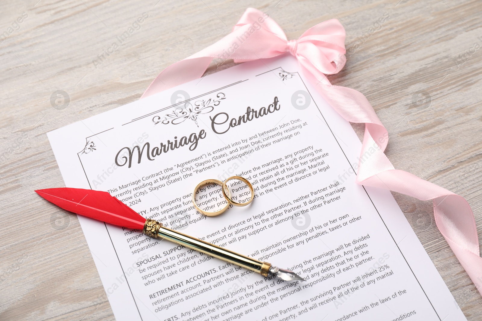 Photo of Marriage contract, ribbon, pen and golden rings on light wooden table, above view