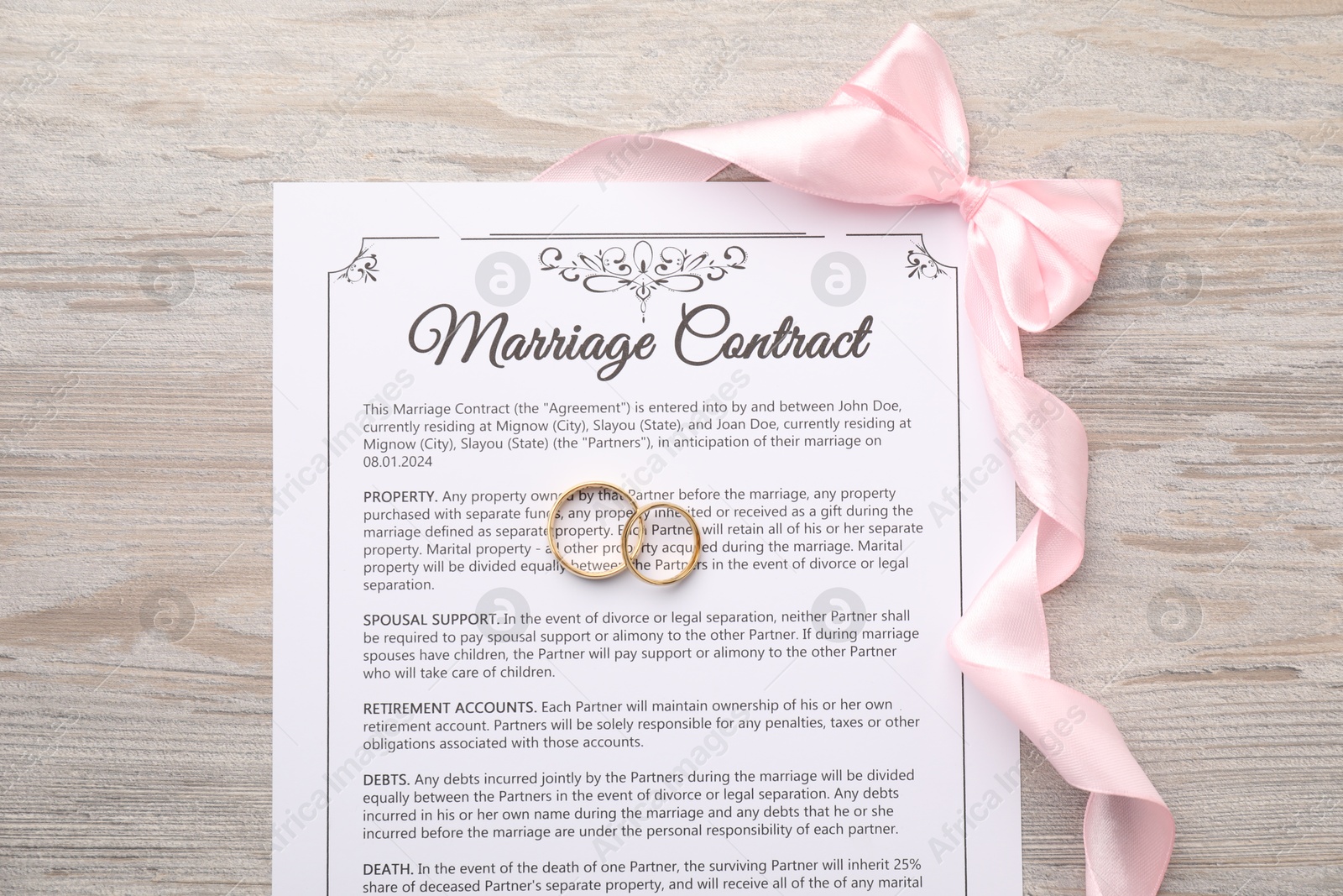 Photo of Marriage contract, ribbon and golden rings on wooden table, top view