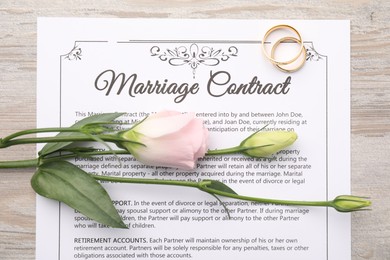 Marriage contract, flowers and golden rings on wooden table, top view