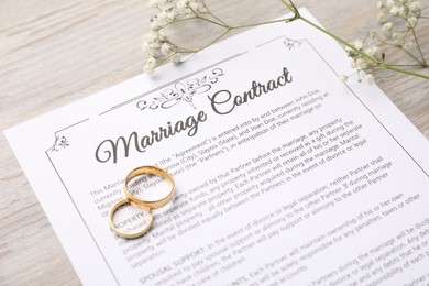 Photo of Marriage contract, flowers and golden rings on wooden table, closeup