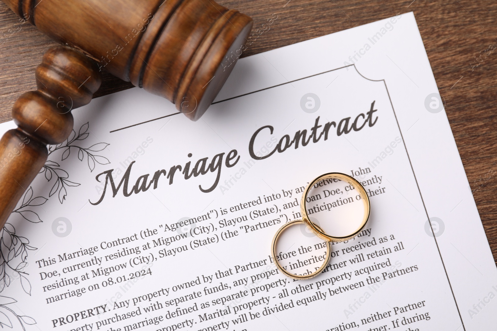 Photo of Marriage contract, gavel and golden rings on wooden table, top view