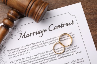 Photo of Marriage contract, gavel and golden rings on wooden table, top view