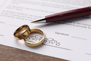 Marriage contract, pen and golden rings on wooden table, closeup