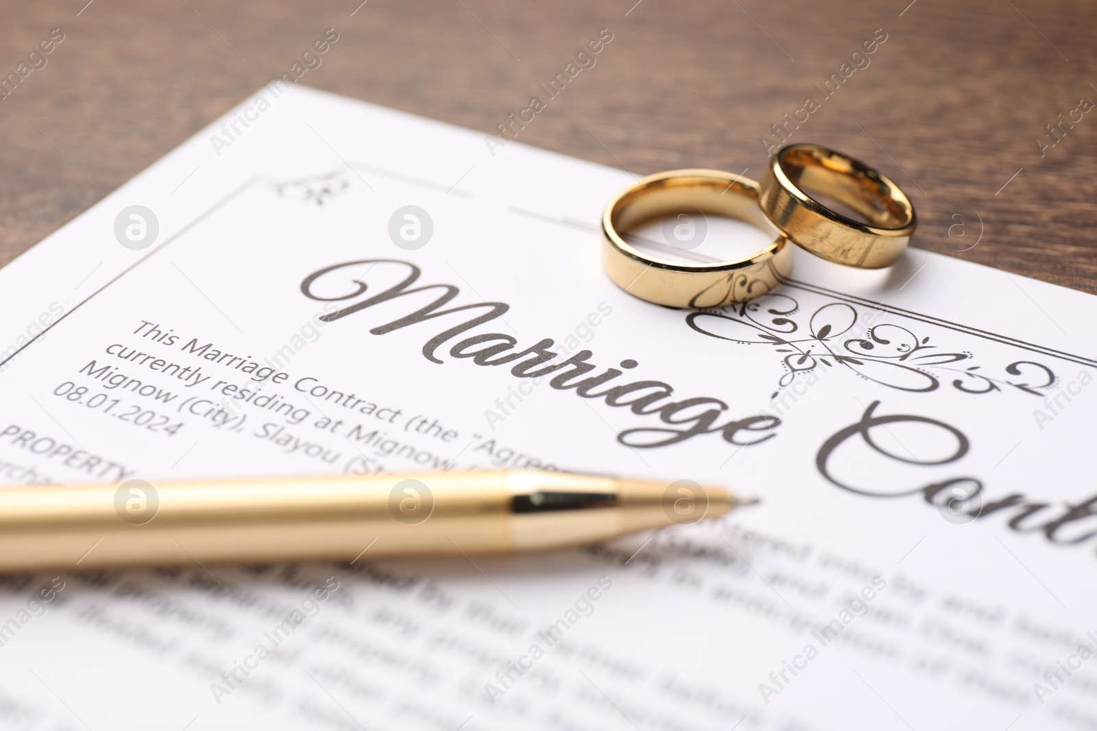 Photo of Marriage contract, pen and golden rings on wooden table, closeup