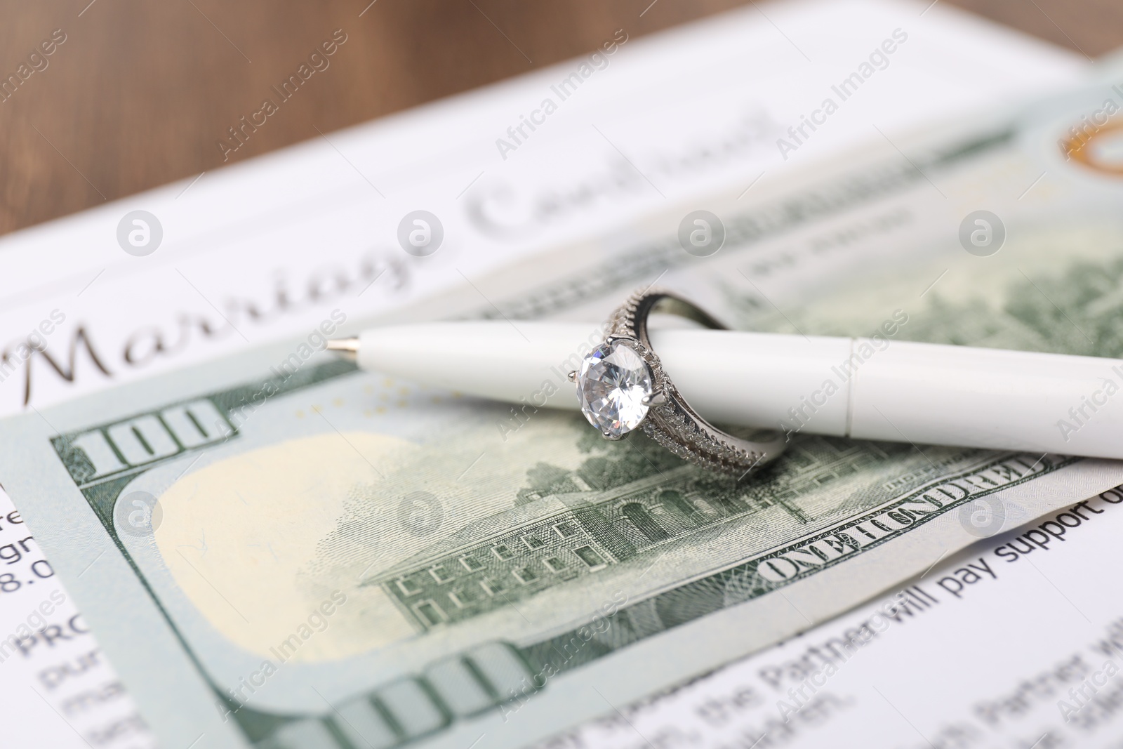 Photo of Marriage contract, dollar bill, pen and ring on wooden table, closeup