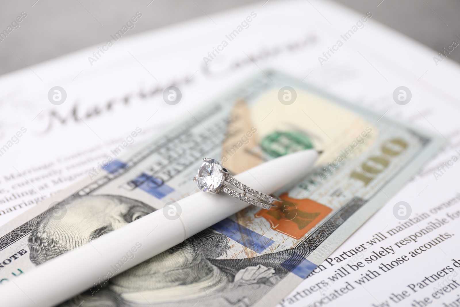 Photo of Marriage contract, pen with ring and dollar bill on grey table, closeup