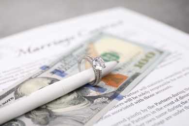 Photo of Marriage contract, pen with ring and dollar bill on grey table, closeup