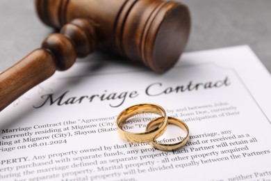 Photo of Marriage contract, gavel and golden rings on grey table, closeup