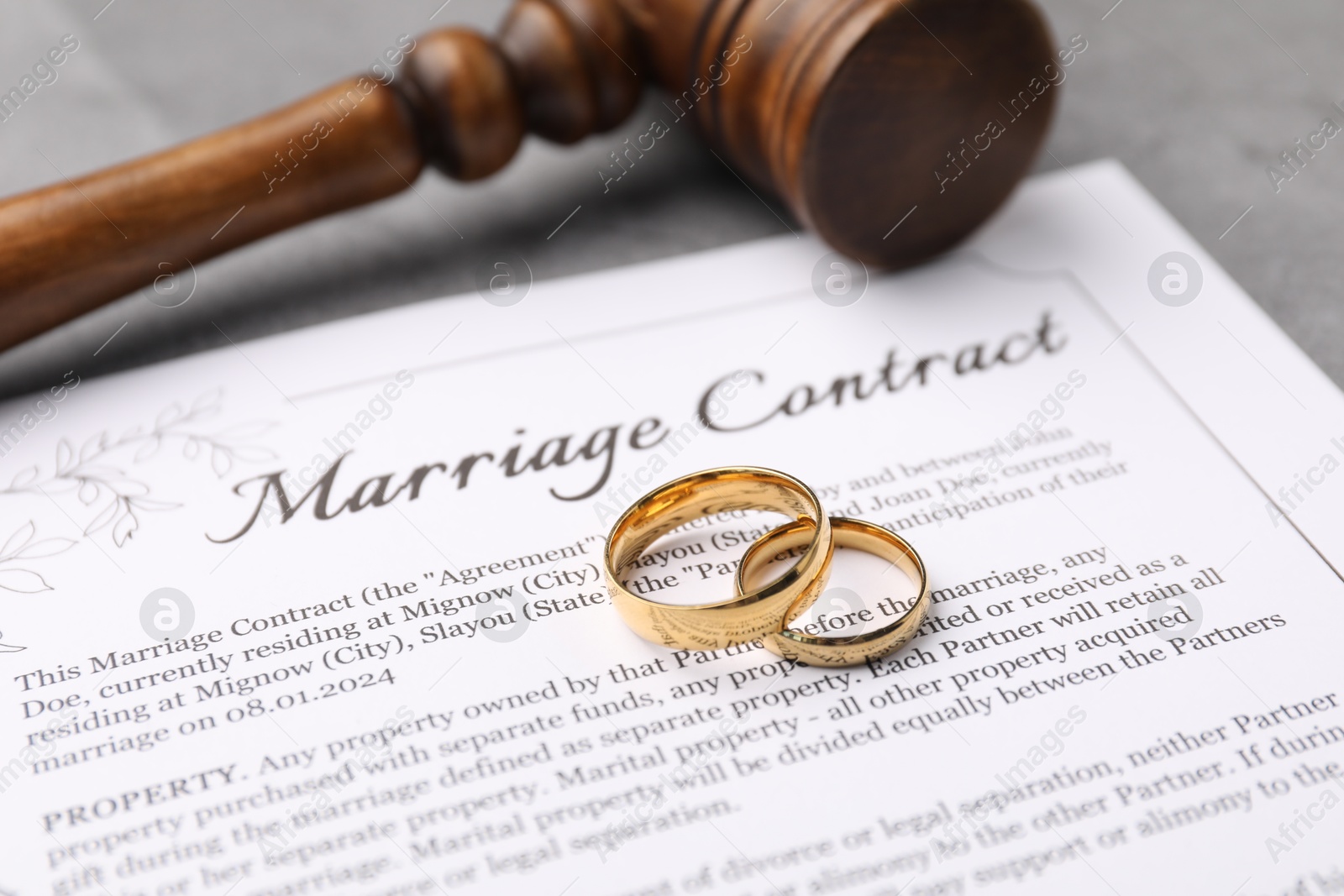 Photo of Marriage contract, gavel and golden rings on grey table, closeup