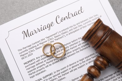 Marriage contract, gavel and golden rings on grey table, top view