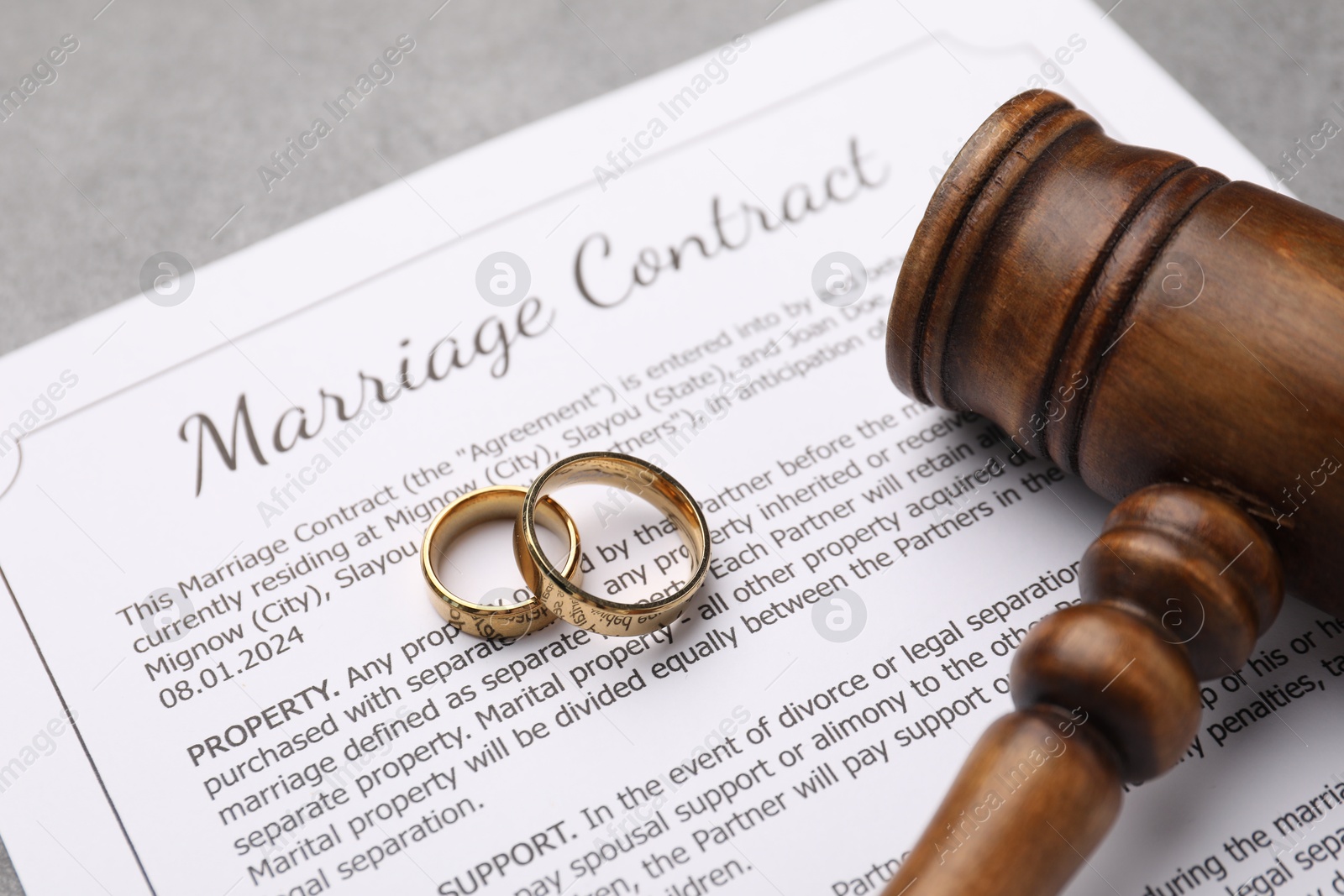 Photo of Marriage contract, gavel and golden rings on grey table, closeup