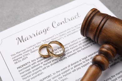 Photo of Marriage contract, gavel and golden rings on grey table, closeup