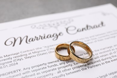 Marriage contract and golden rings on grey table, closeup