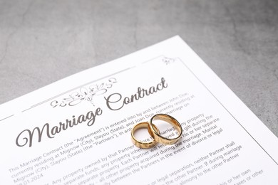 Photo of Marriage contract and golden rings on grey table, closeup