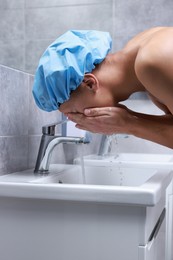 Man wearing shower cap washing his face in bathroom