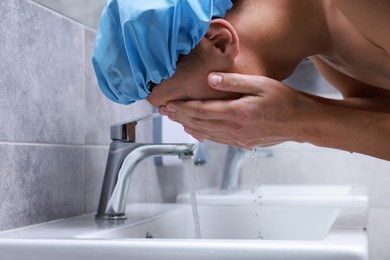 Man wearing shower cap washing his face in bathroom