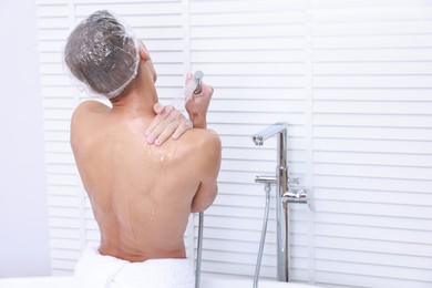 Photo of Man in cap taking shower in bathroom, back view