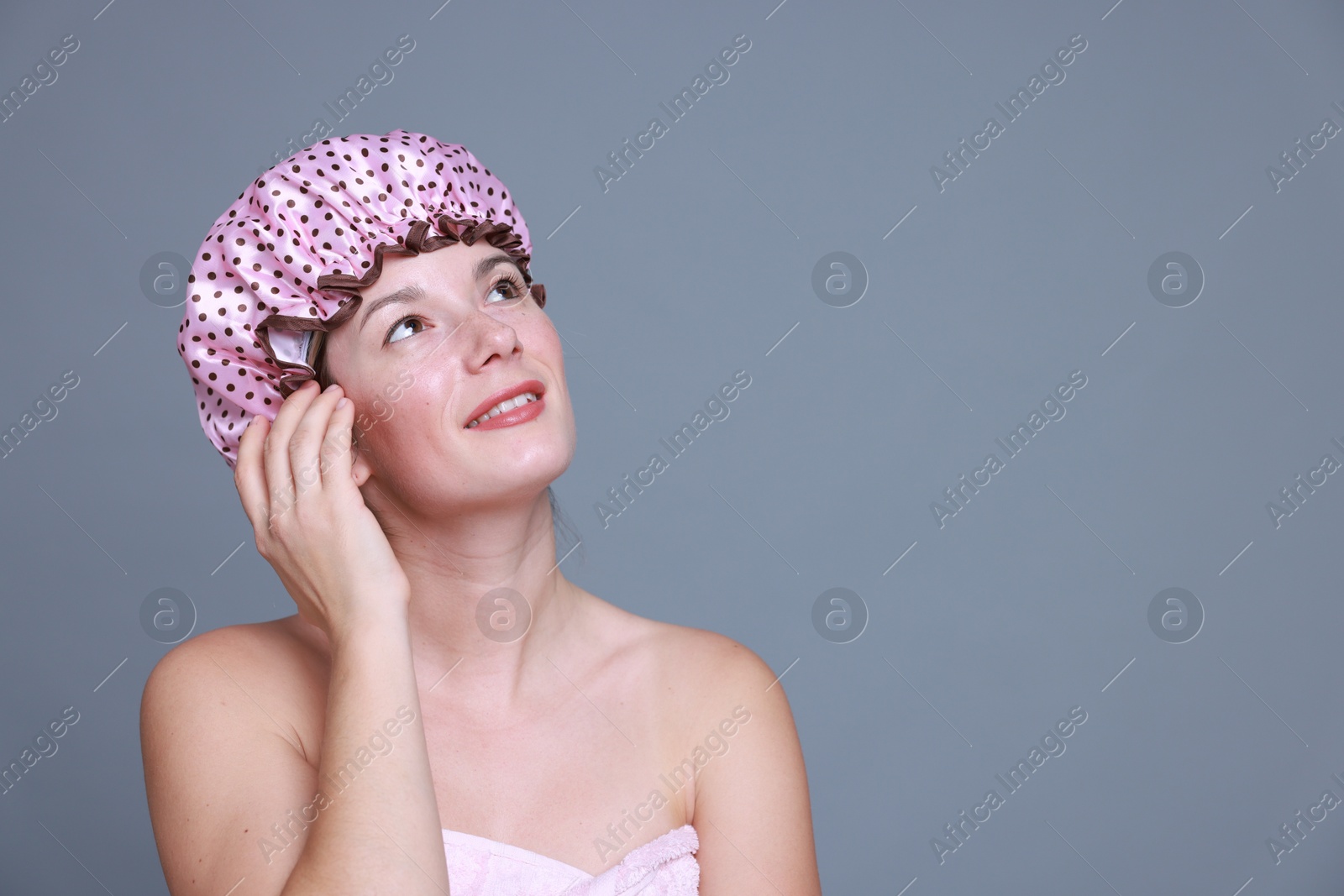 Photo of Happy woman in shower cap on grey background, space for text