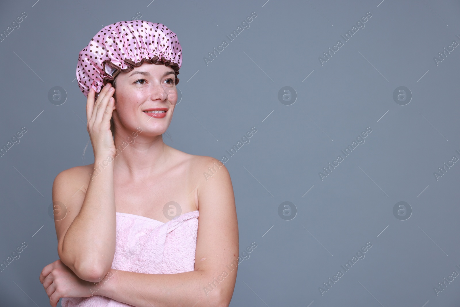 Photo of Happy woman in shower cap on grey background, space for text