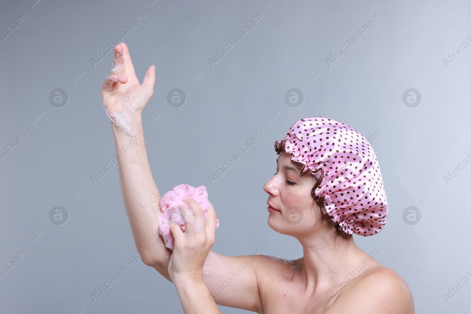 Photo of Woman with shower cap and mesh sponge on grey background