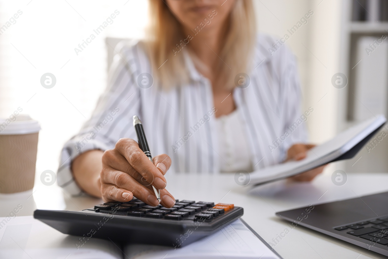 Photo of Budget planning. Woman with notebook using calculator at table indoors, closeup