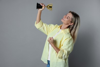 Photo of Happy winner with golden trophy cup on gray background, space for text