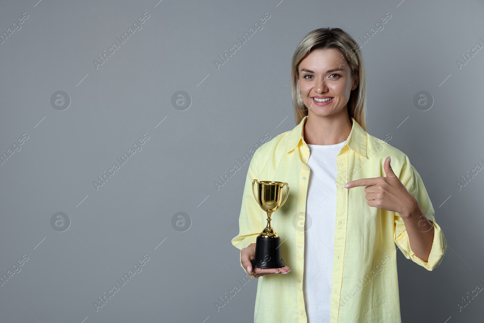 Photo of Happy winner with golden trophy cup on gray background, space for text