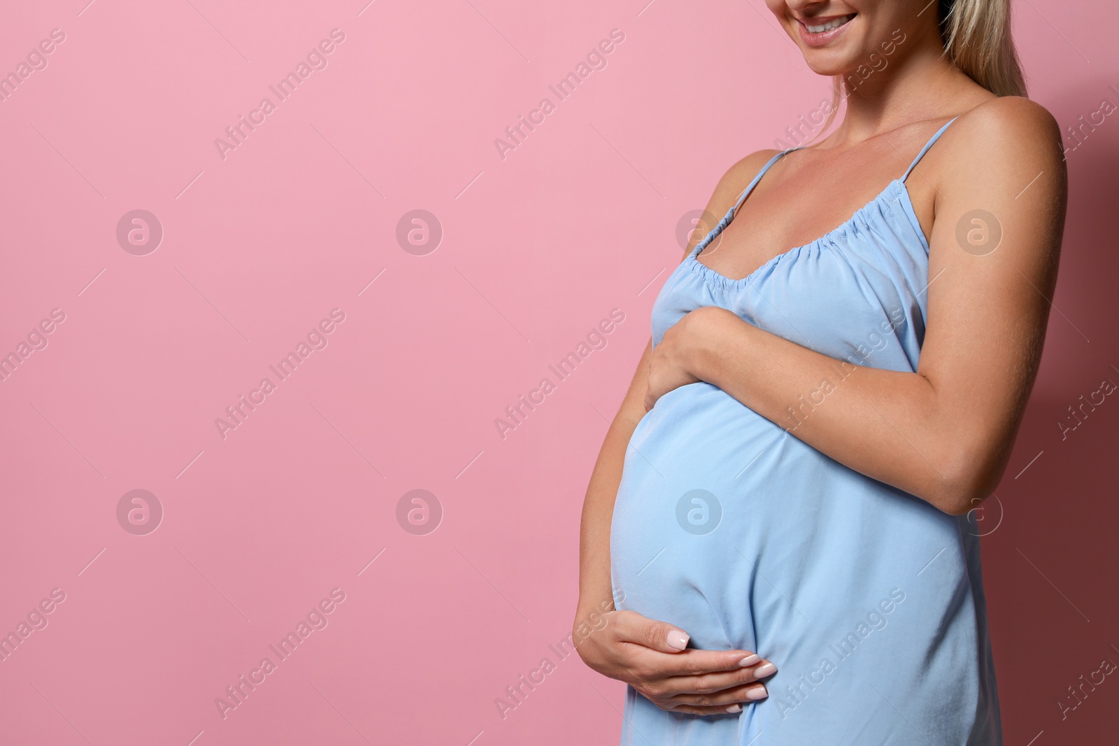 Photo of Pregnant woman on pink background, closeup. Space for text