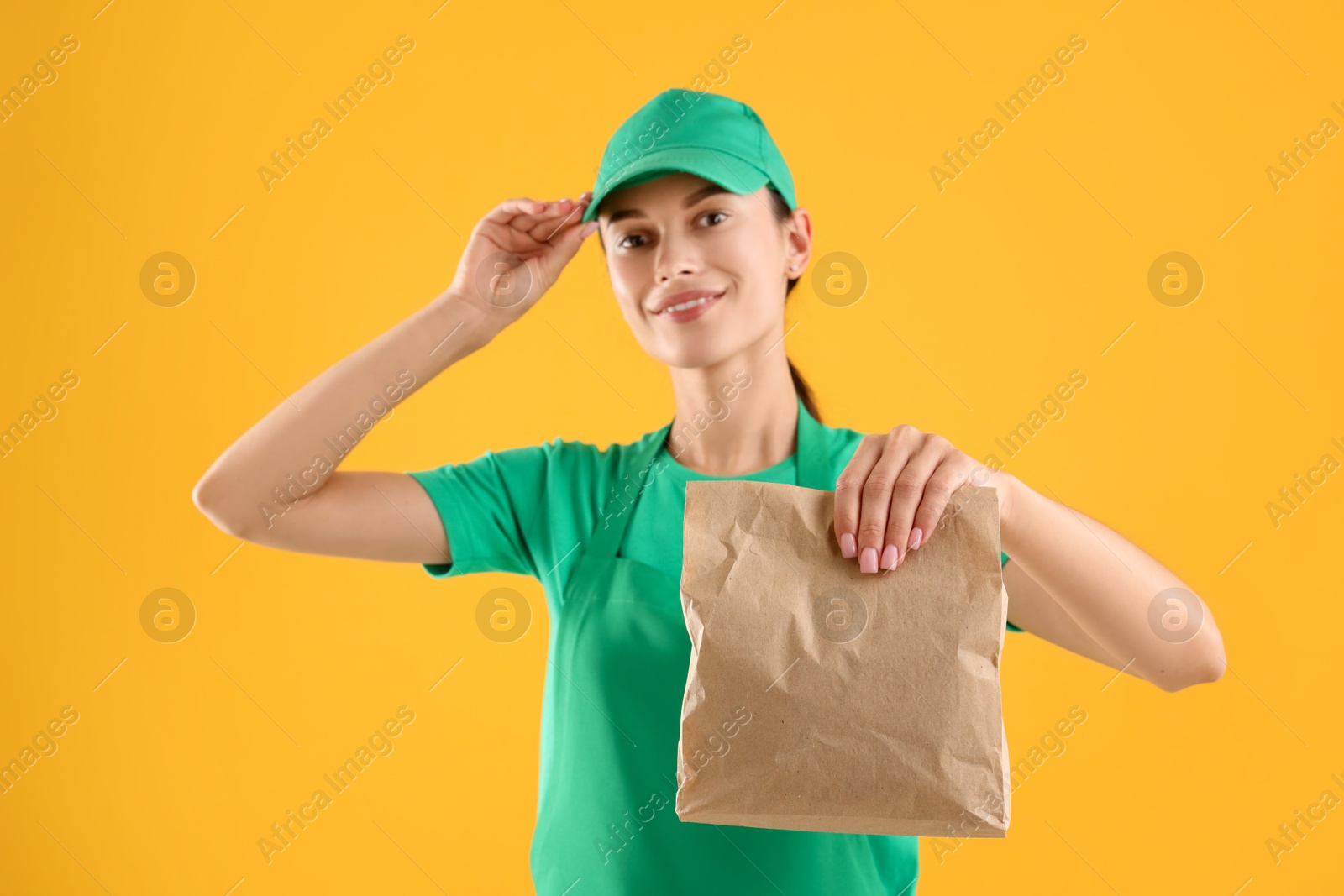 Photo of Fast-food worker with paper bag on orange background, selective focus