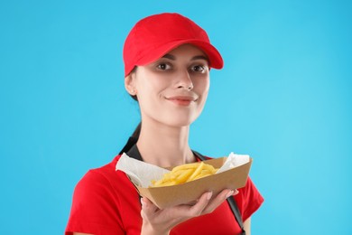 Photo of Fast-food worker holding paper container with fries on light blue background