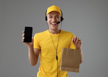 Photo of Fast-food worker with paper bag and smartphone on gray background